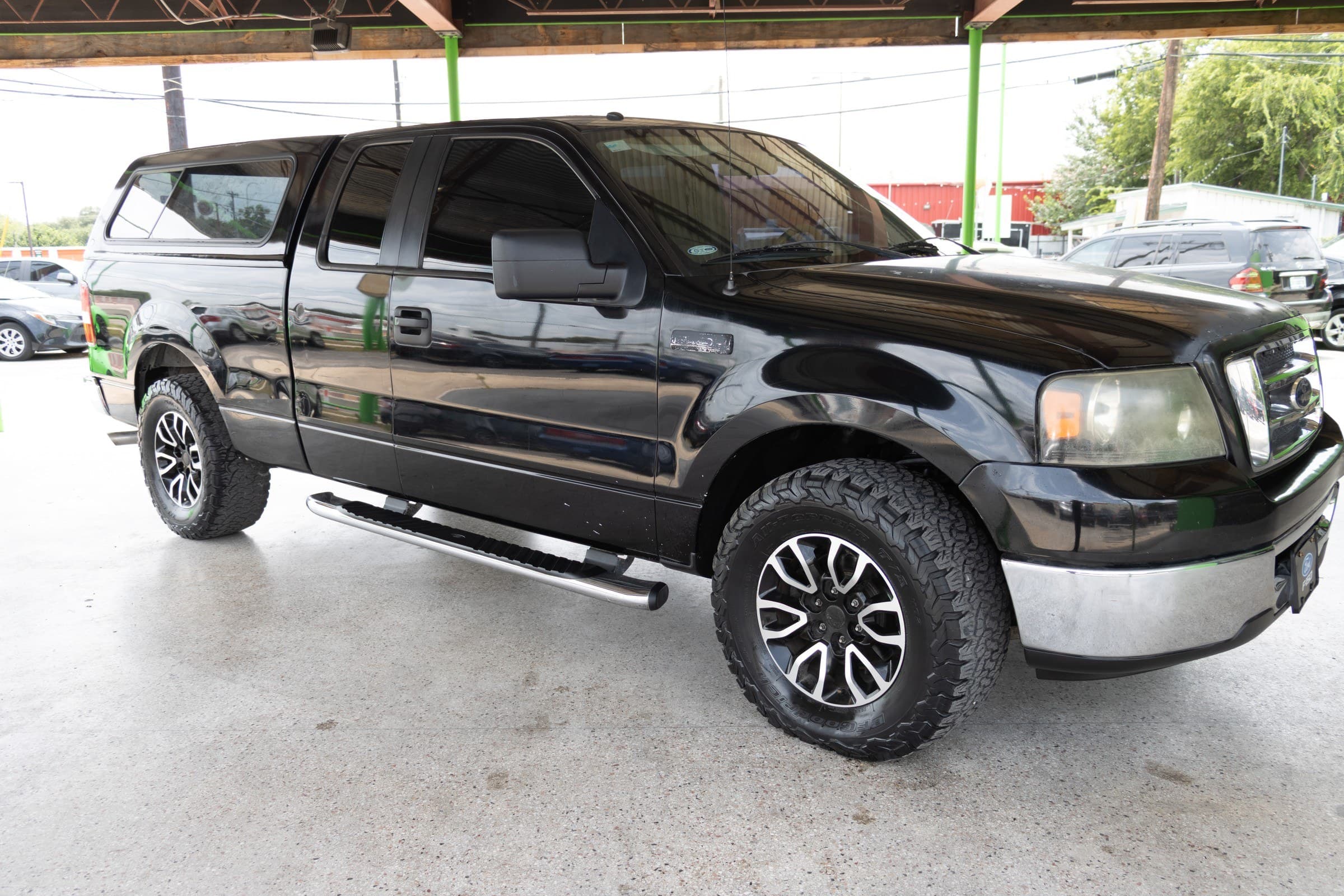 Black 2007 Ford F-150 extended-cab pickup with a matching black camper shell over the bed, seen from the front passenger side.