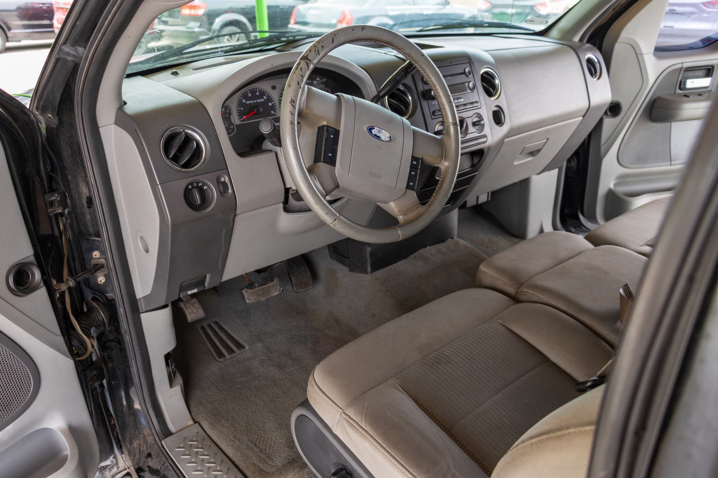 Driver's cockpit of the F-150: gray dashboard, cloth-wrapped steering wheel with cruise control buttons, and tan cloth seats.