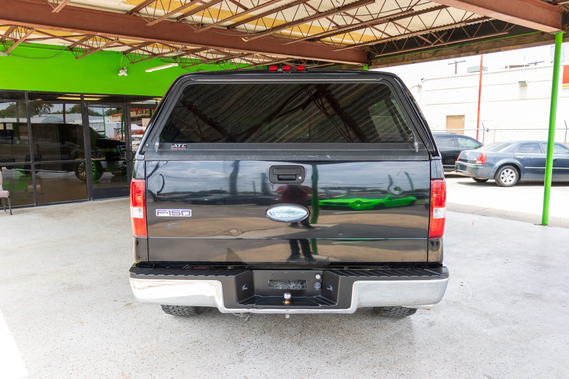 Rear view of the F-150 with the tailgate closed, showing the camper shell's tinted rear window and the chrome rear bumper with a trailer hitch receiver.
