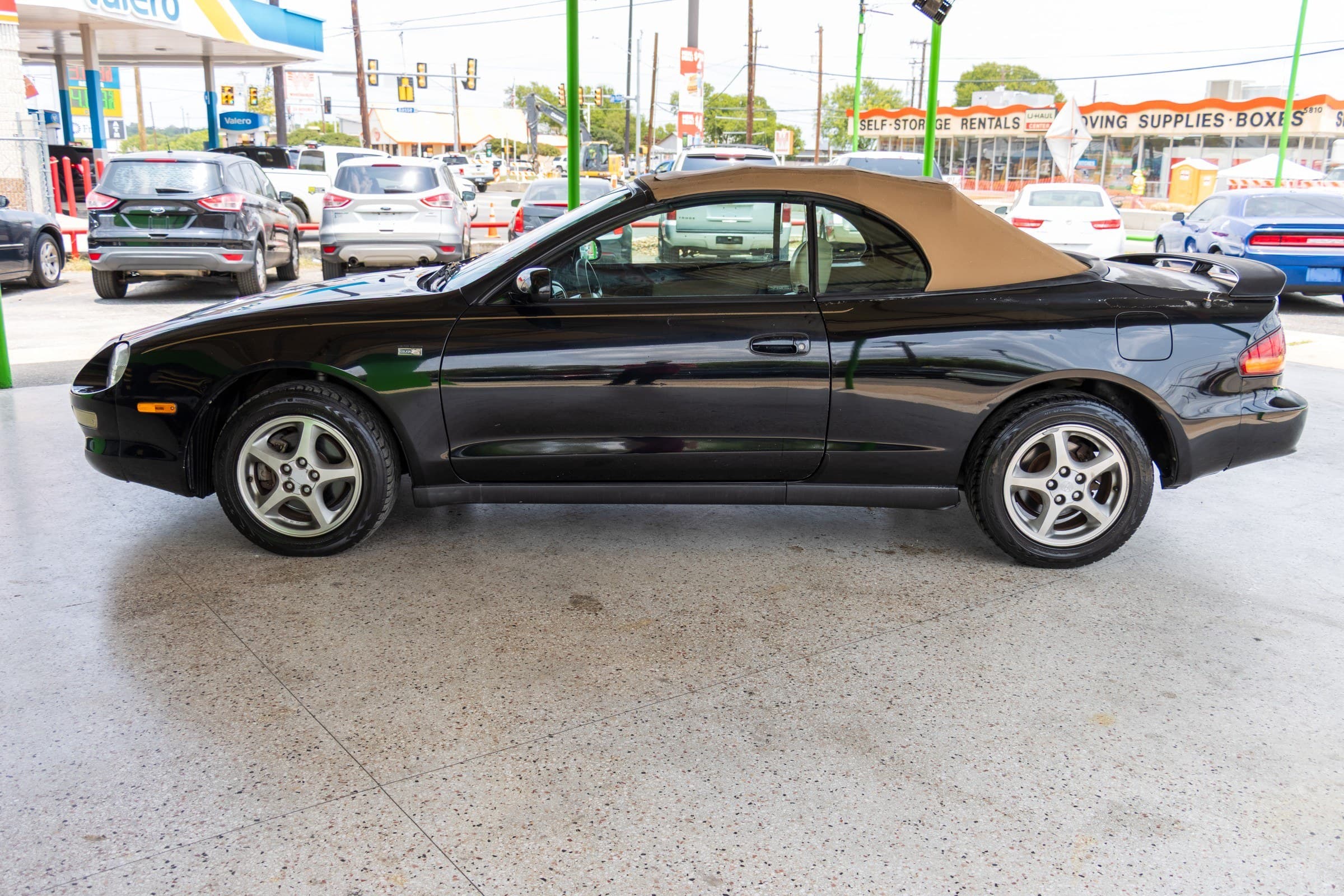 Driver-side profile of the black Celica convertible parked under the Kelley Autoplex canopy.