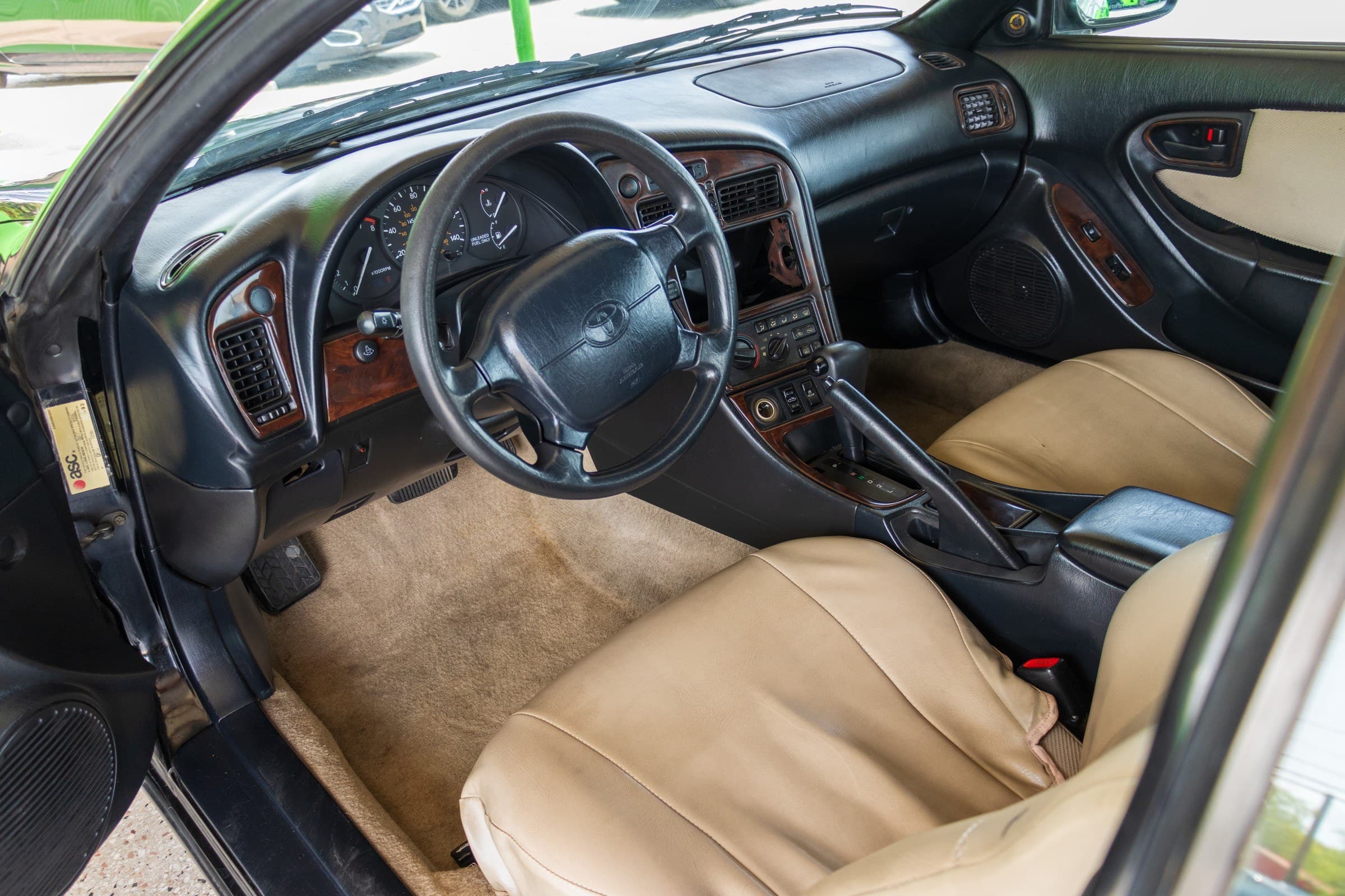 Driver's cockpit of the Celica: black dashboard with wood-grain trim, three-spoke steering wheel and tan leather seats.