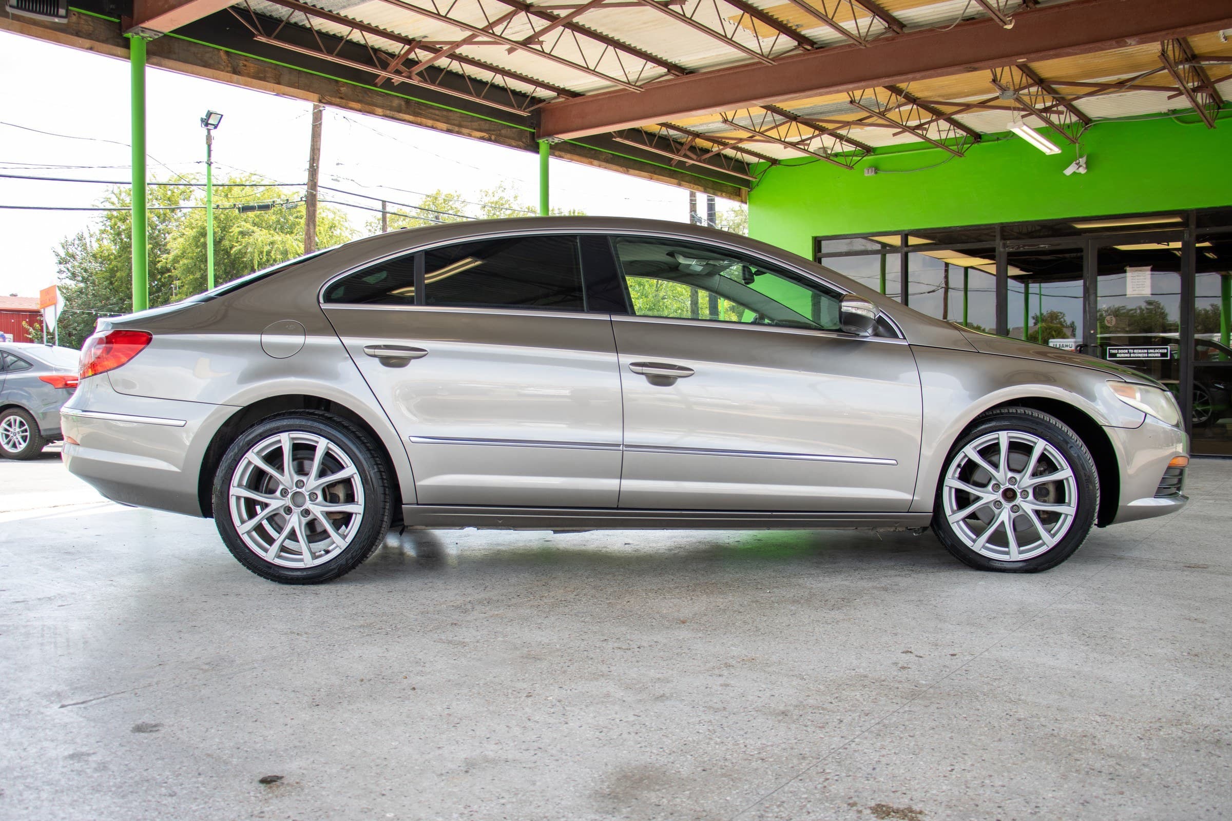 Full passenger-side profile of the brown metallic Volkswagen CC, showing its frameless door windows and silver multi-spoke alloy wheels.