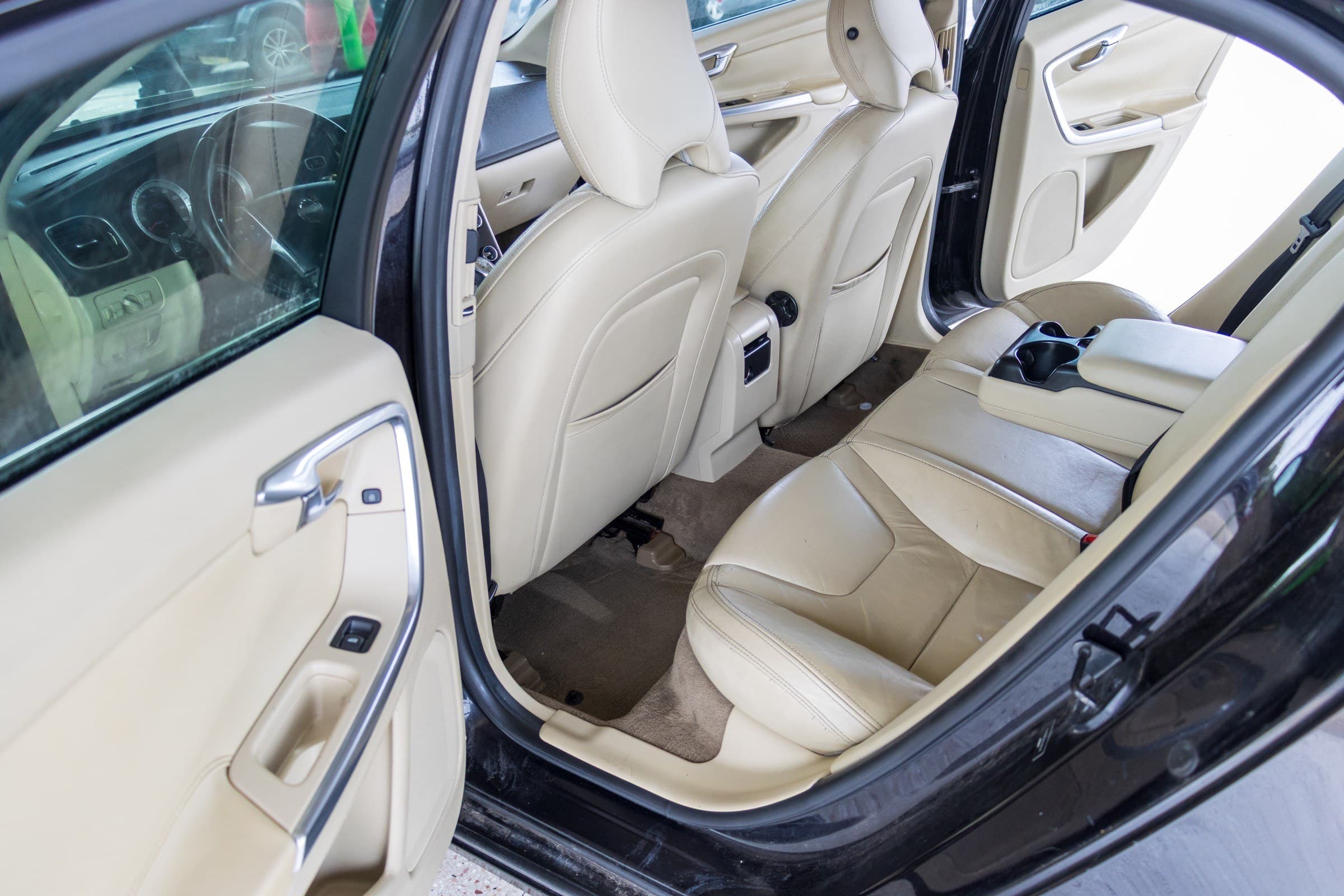 Rear cabin of the S60 seen through the open rear door, showing the tan leather seats and matching door trim.