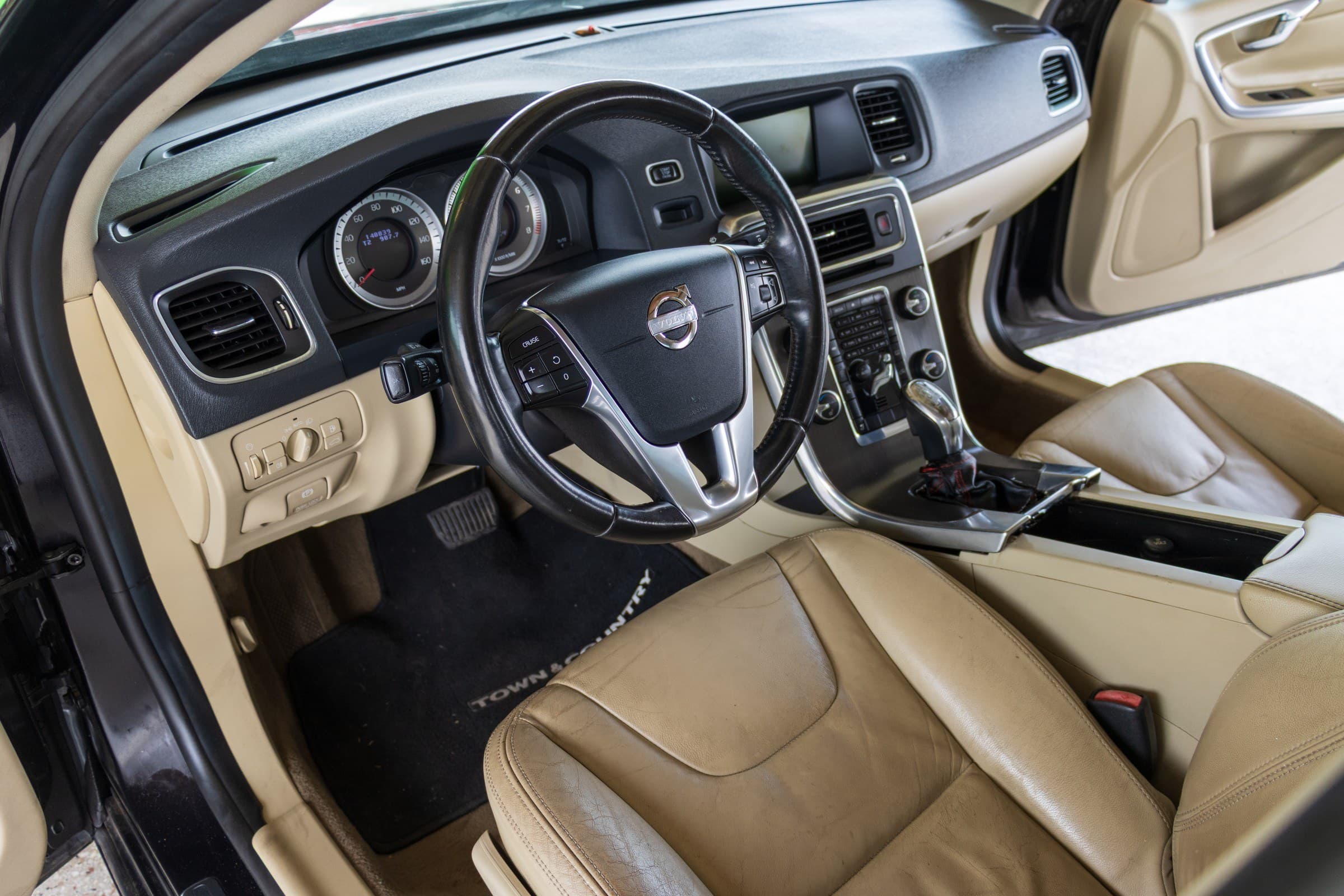 Driver's cockpit of the S60, with a black and tan dashboard and a leather steering wheel; the odometer reads 148,839 miles.