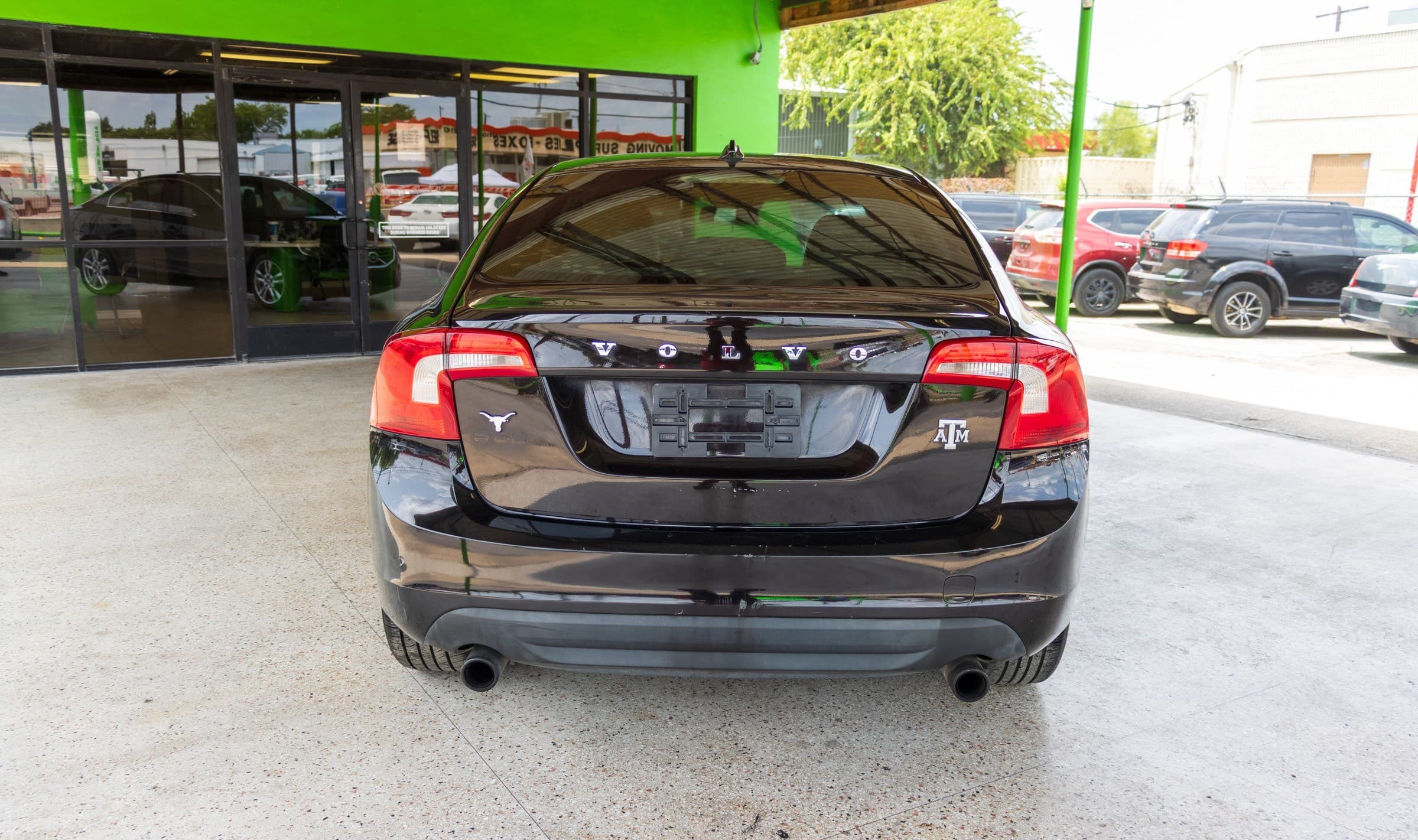 Rear view of the black Volvo S60, showing the VOLVO lettering across the trunk and Texas Longhorns and Texas A&M emblems.