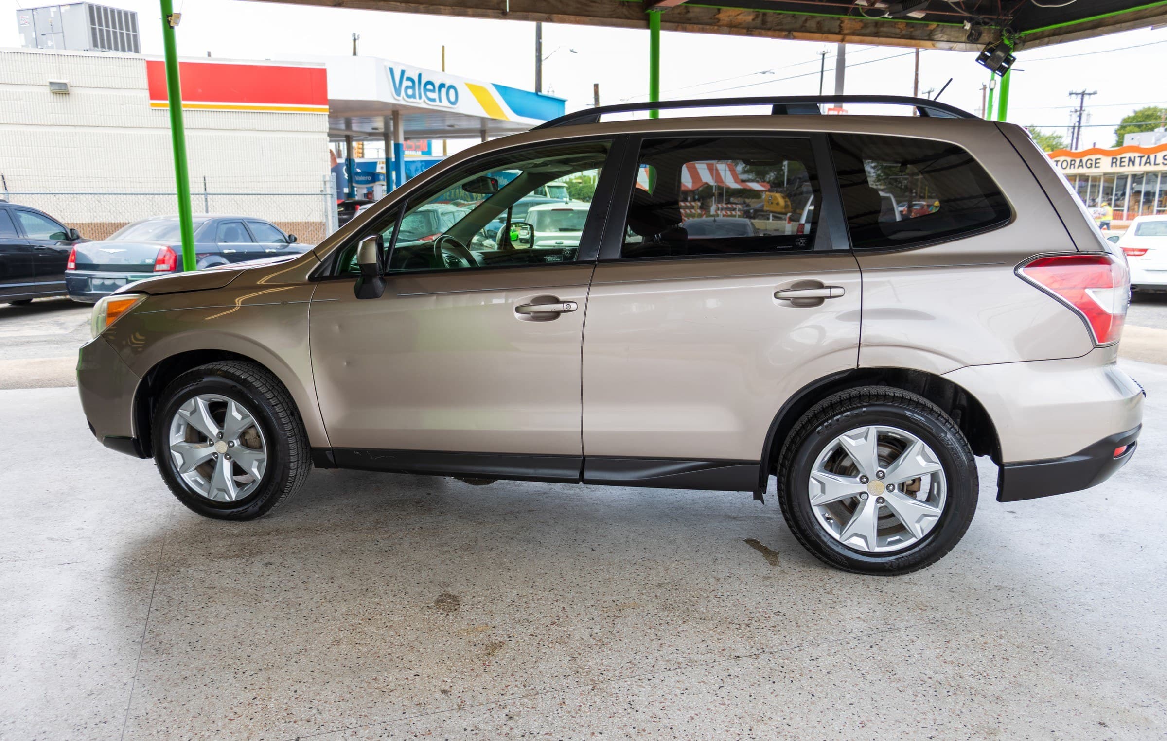 Full driver-side profile of the bronze Subaru Forester parked under the Kelley Autoplex canopy.