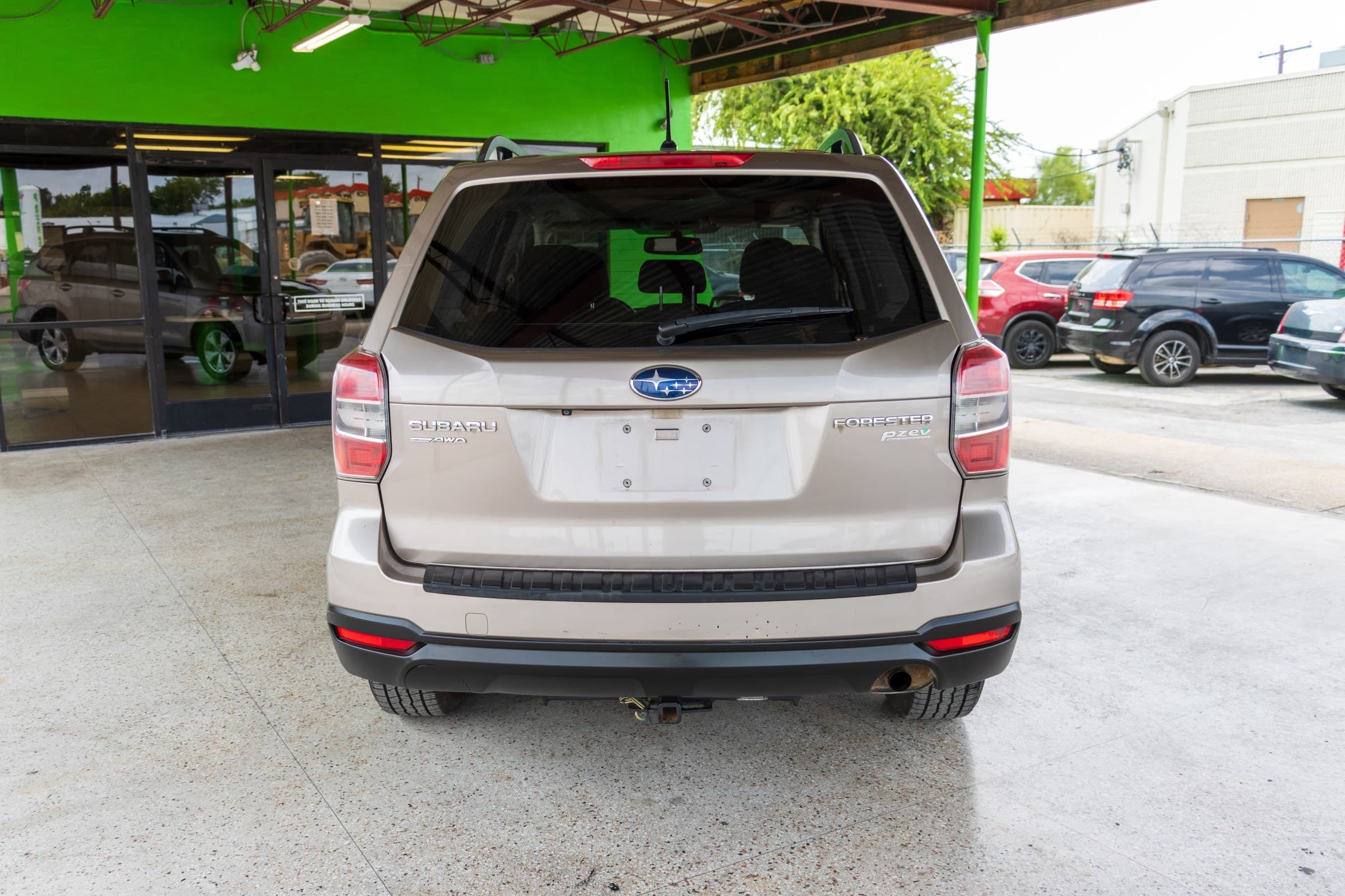 Rear view of the Forester with the tailgate closed, showing the Subaru, AWD, Forester and PZEV badges and a trailer hitch receiver below the bumper.