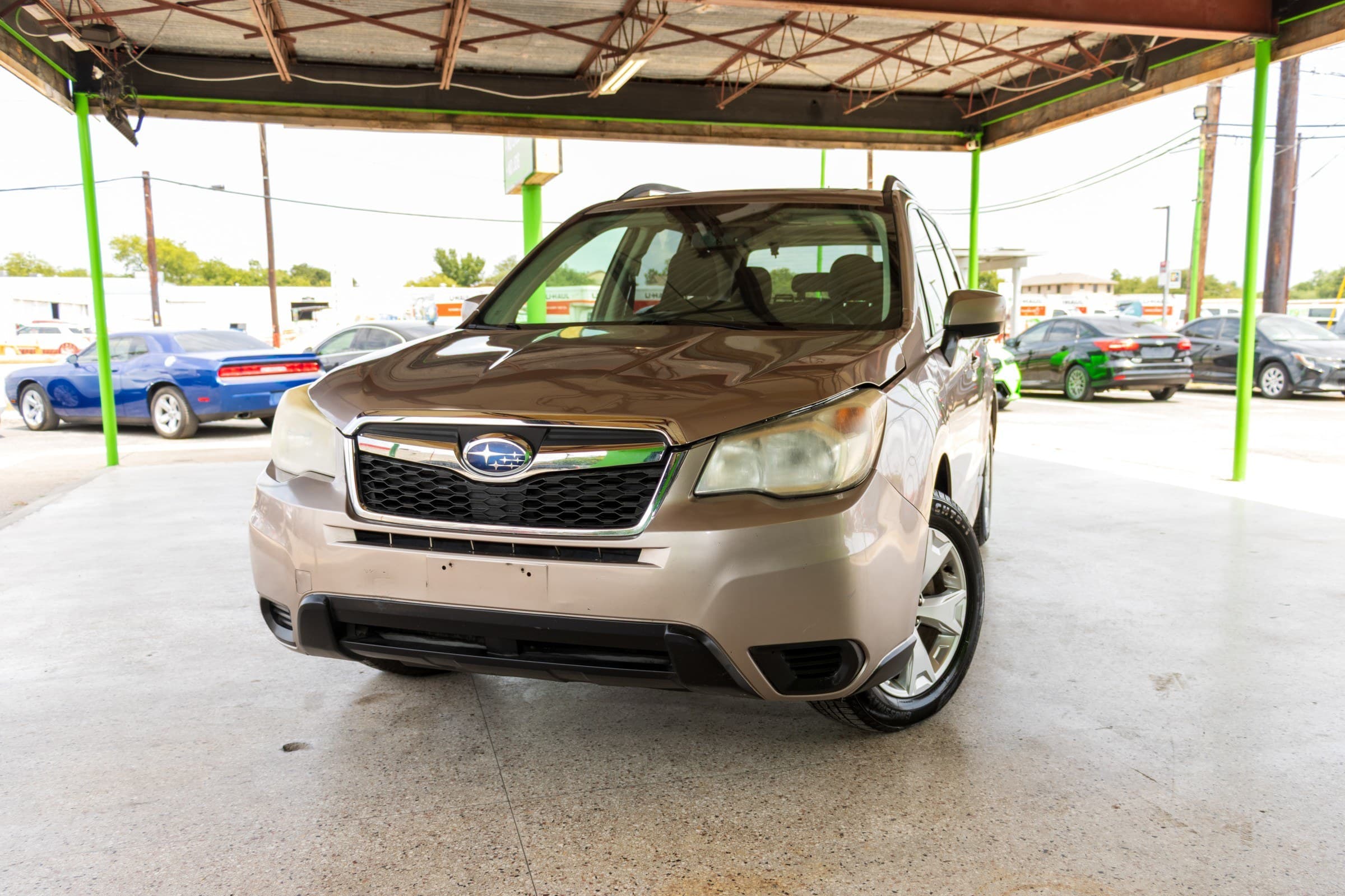 Bronze metallic 2014 Subaru Forester seen from a low front angle, showing the chrome grille surround, Subaru badge and roof rails.