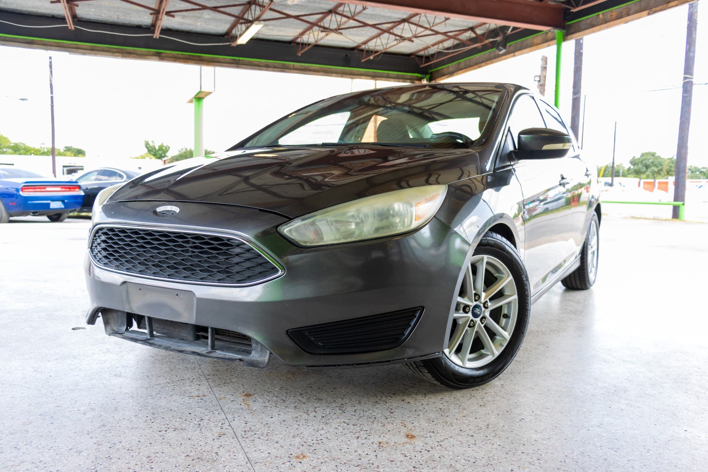 Gray 2016 Ford Focus SE sedan seen from a low front driver-side angle, showing the black mesh grille and silver alloy wheels.