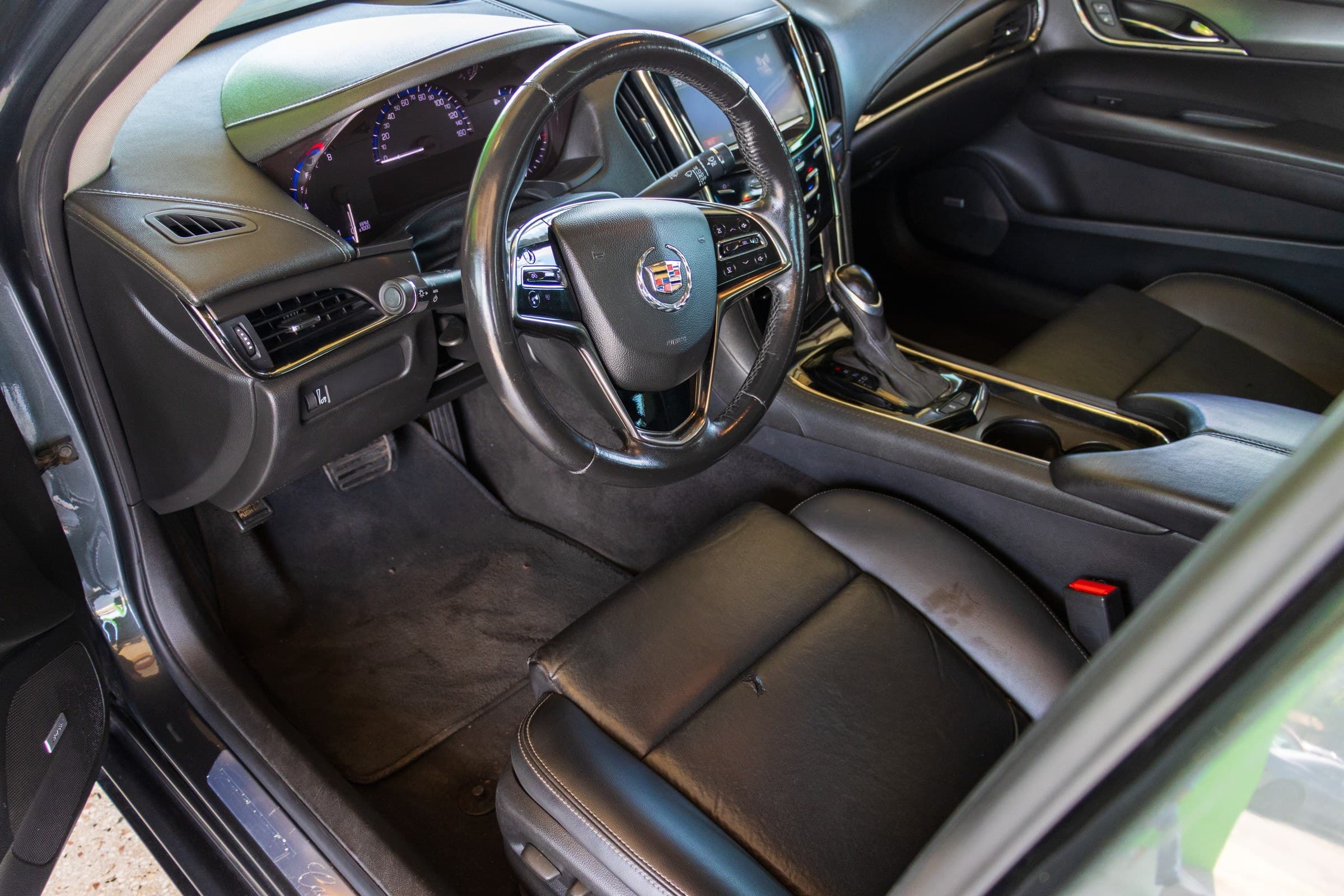 Driver's cockpit of the ATS: black leather seats, leather-wrapped steering wheel and the CUE touchscreen in the centre stack.