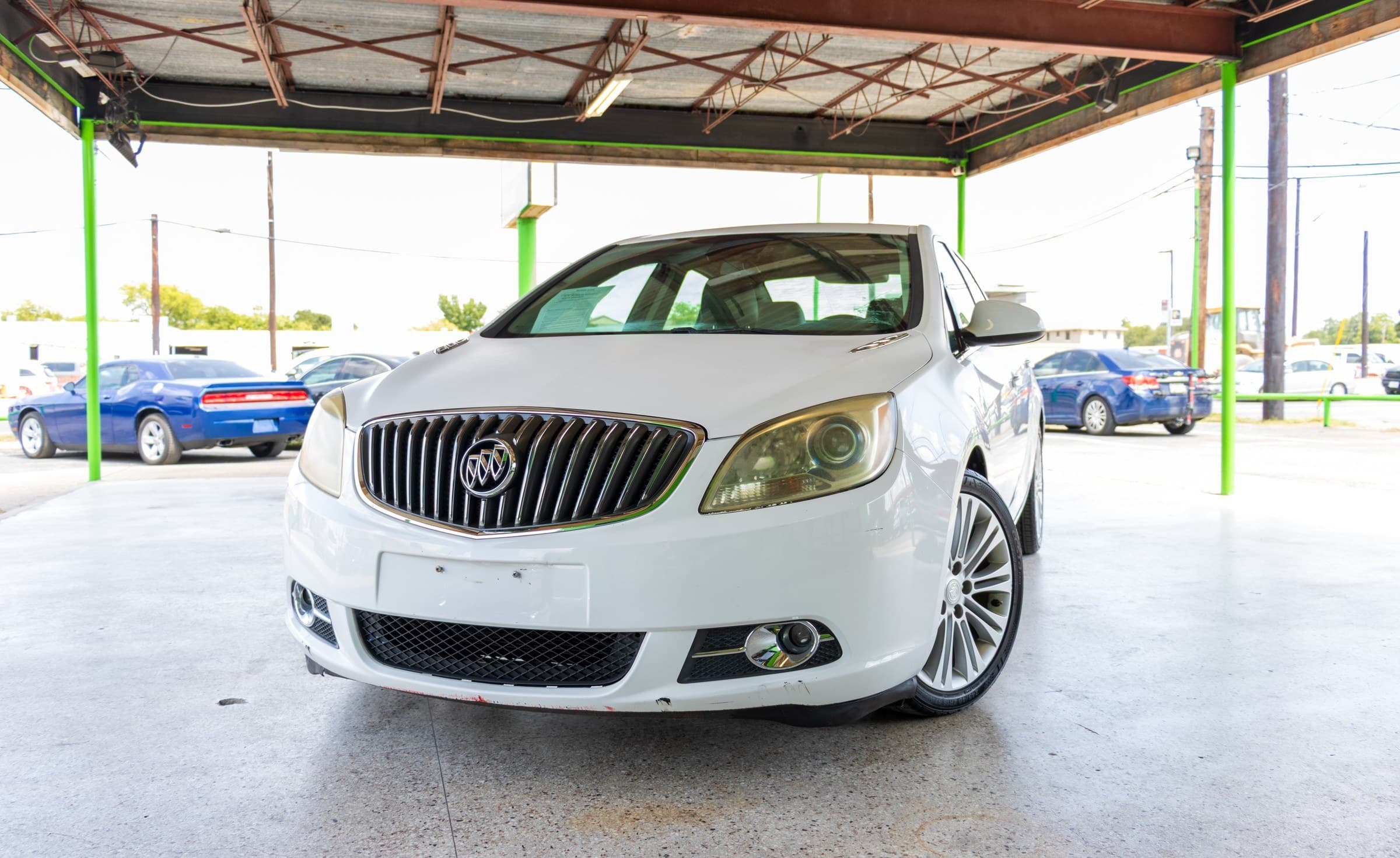 White 2013 Buick Verano seen head-on from a low front angle, showing the chrome waterfall grille and Buick badge.