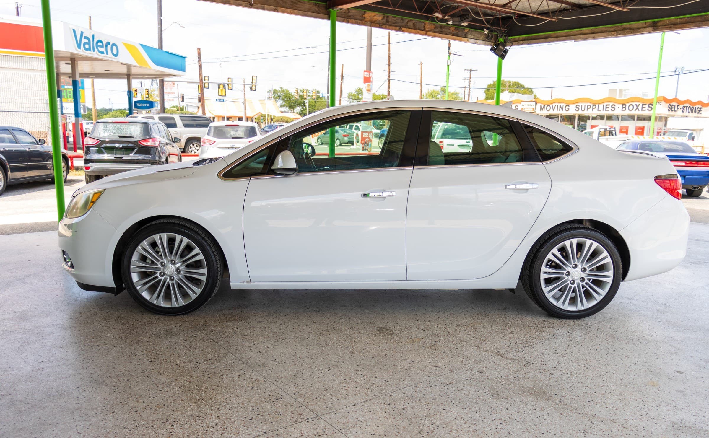 Full driver-side profile of the white Buick Verano parked under the Kelley Autoplex canopy.